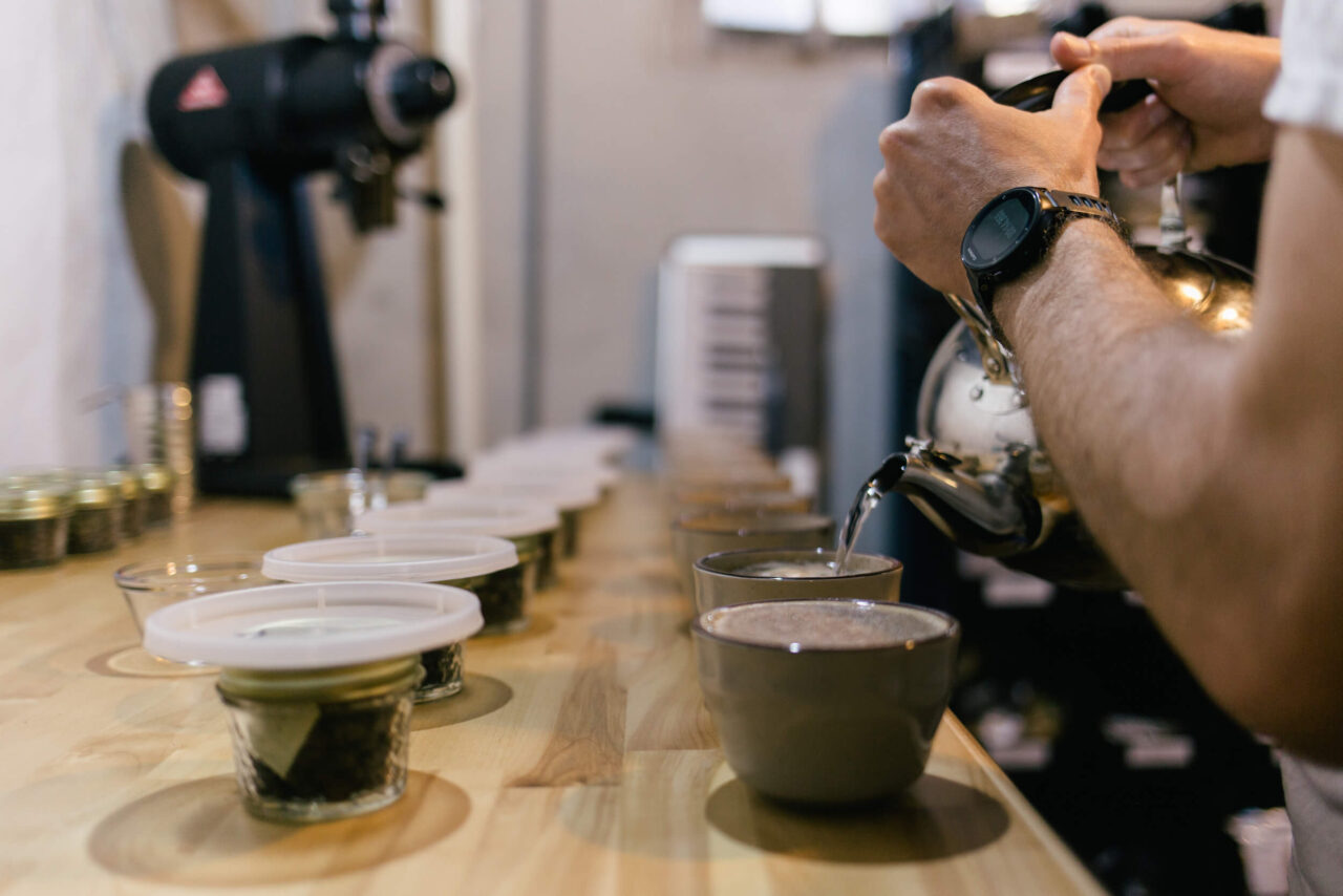 Person pouring water from a kettle into cups of coffee