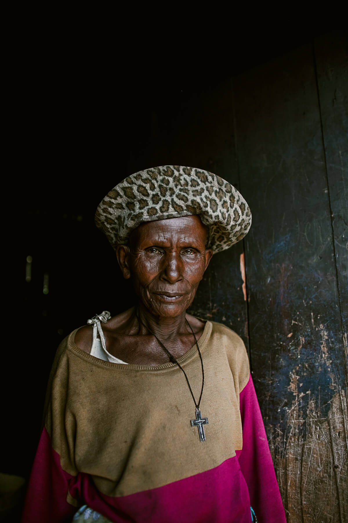 Older woman wearing leopard print hat and crucifix starting directly at the camera