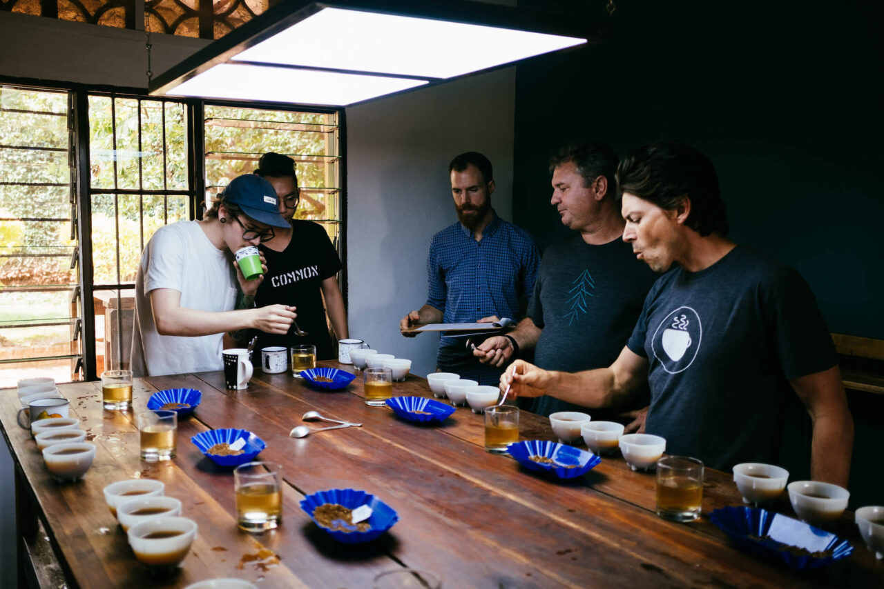 People around a wooden table cupping coffees