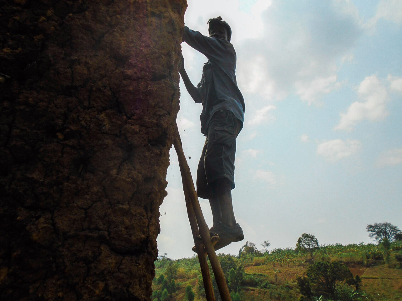 Burundian man standing on a ladder leaning against a house