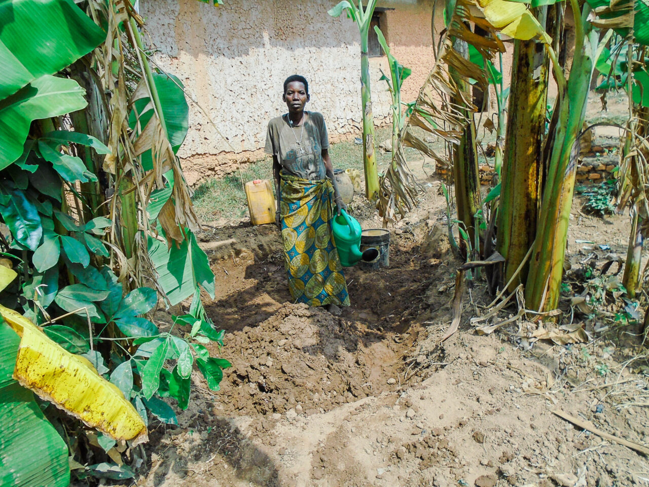 A Burundian woman water vegetables growing outside her father's home