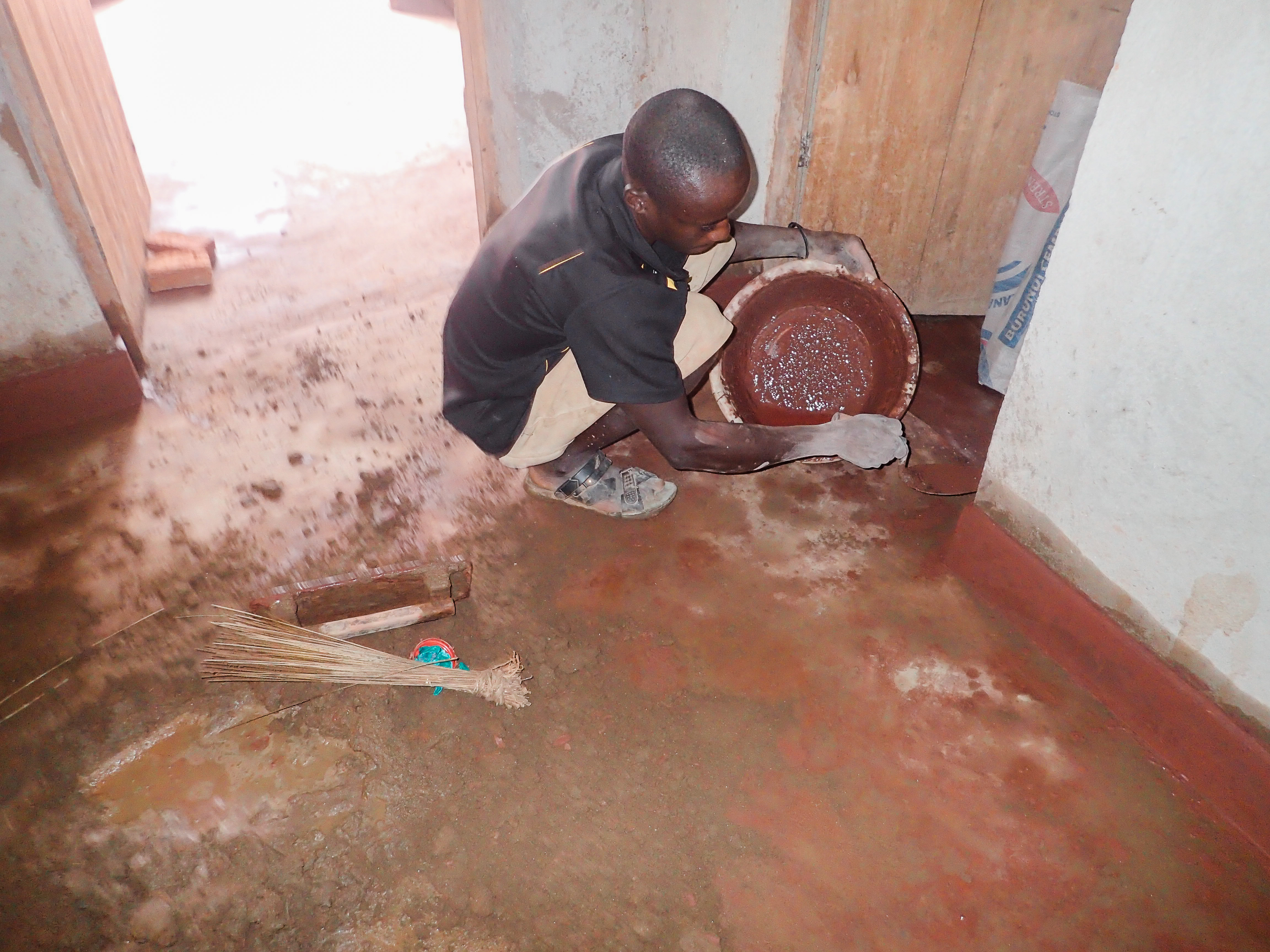 A Burundian man pouring the cement floors of a newly-built house.